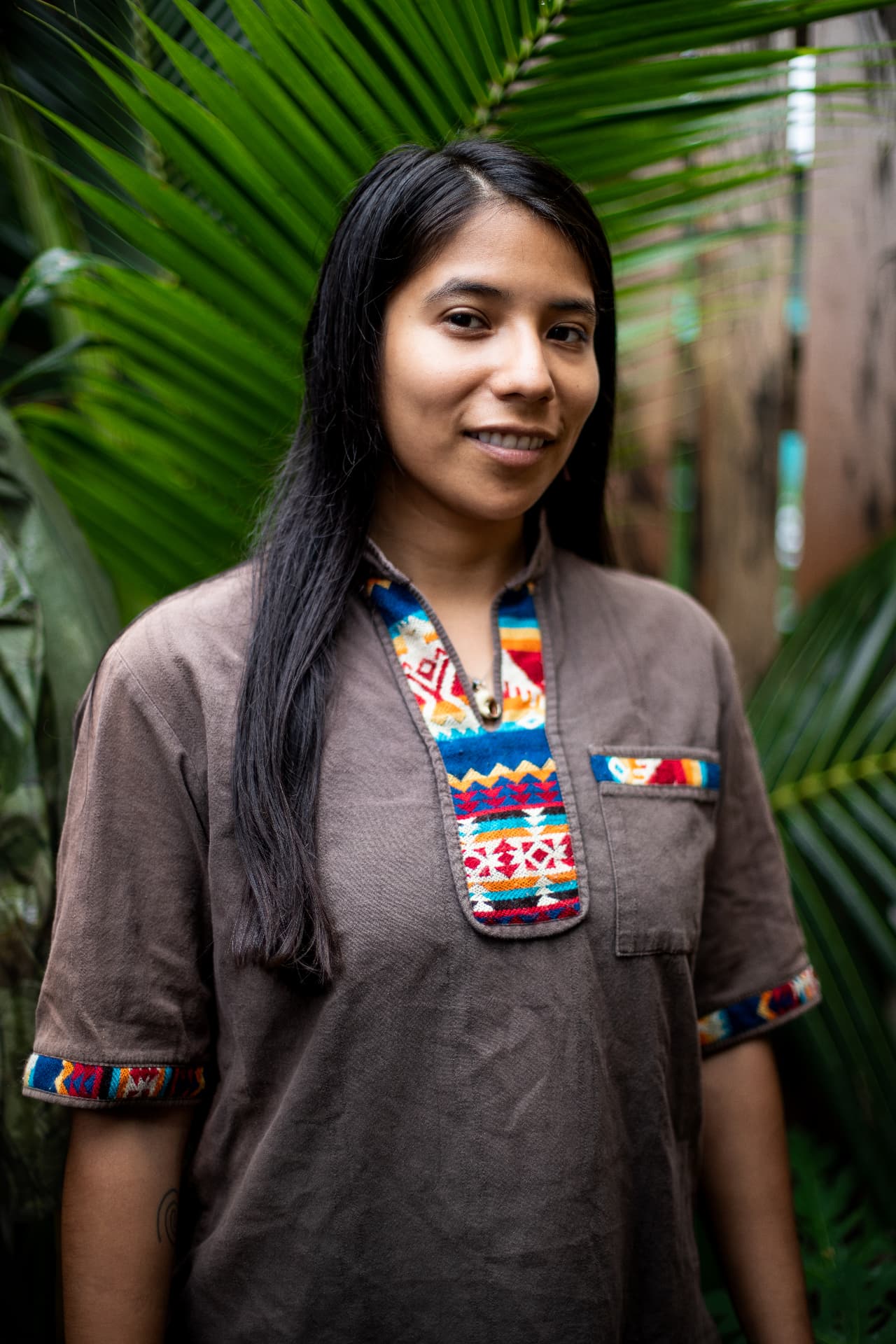 Close portrait of Yura Sapi wearing a patterned garment, with palm leaves behind