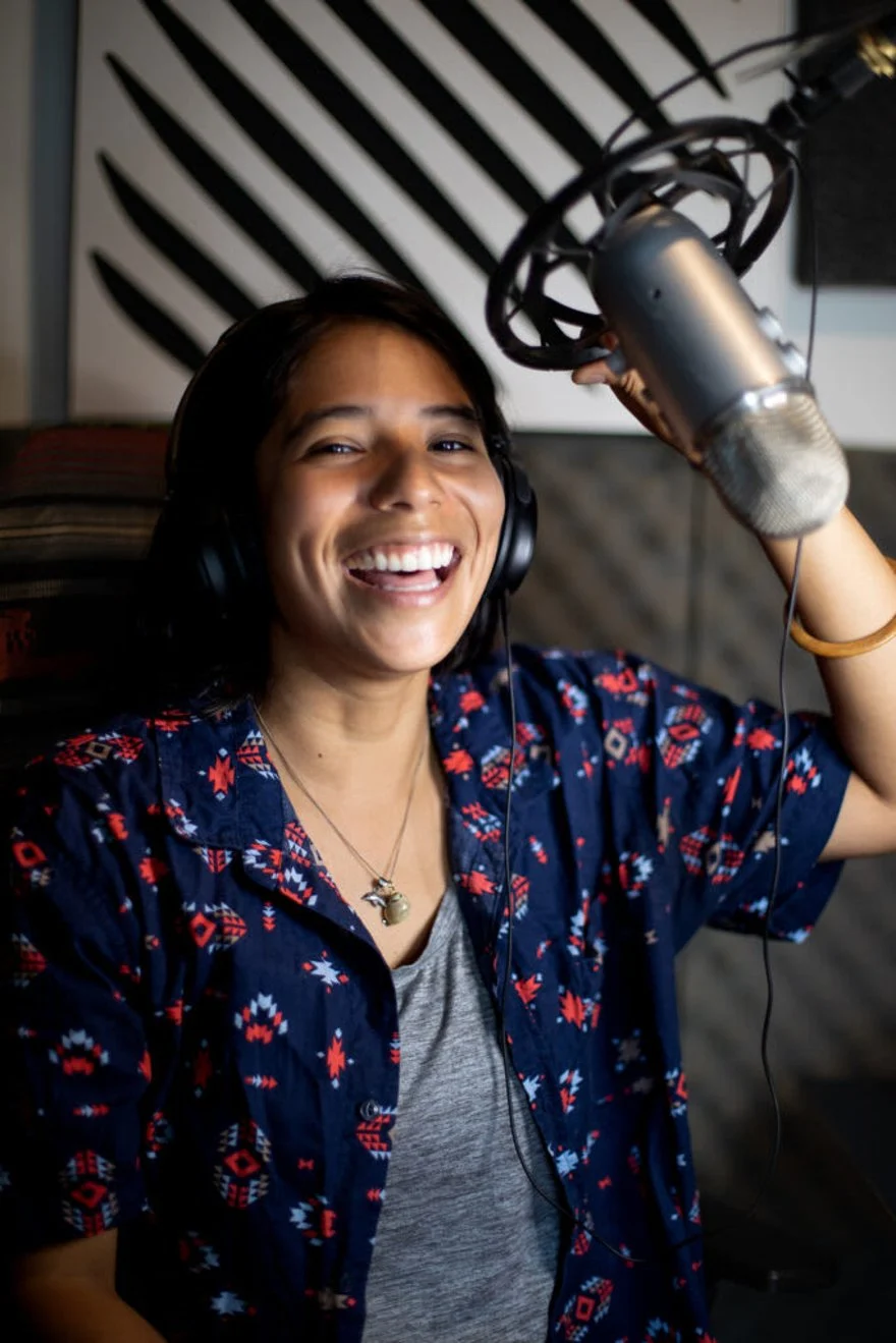 Yura Sapi smiling in a recording studio, wearing headphones and holding a microphone