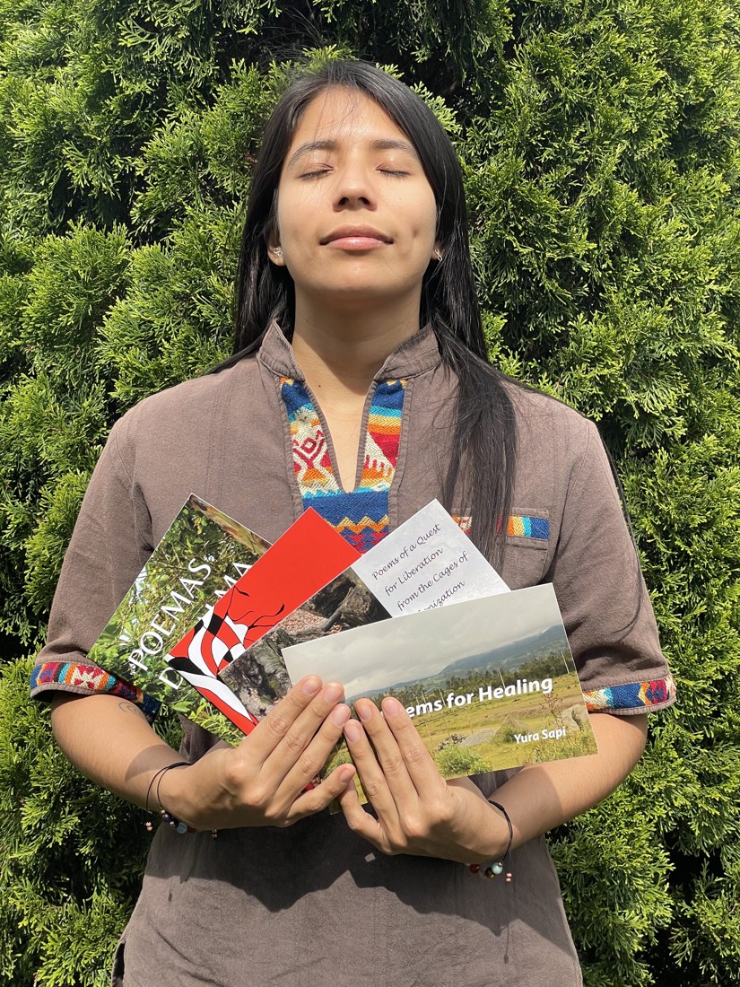 Yura Sapi with their poetry collections in a green outdoor setting